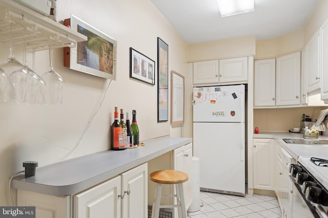 kitchen with a sink, white cabinets, range with gas stovetop, light countertops, and freestanding refrigerator