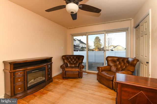 living area featuring light wood-style floors, ceiling fan, baseboards, and a glass covered fireplace