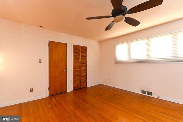 unfurnished bedroom with two closets, visible vents, ceiling fan, wood finished floors, and baseboards