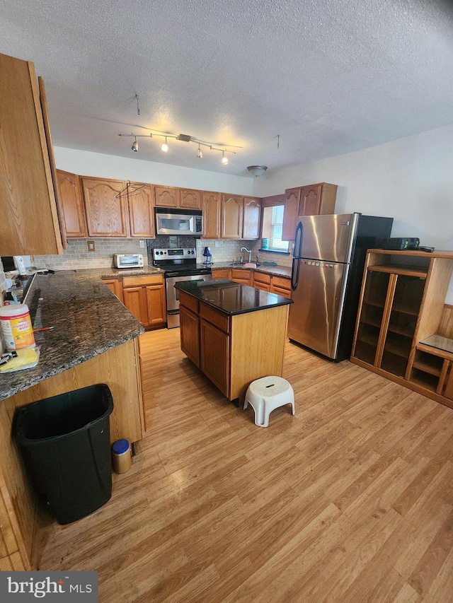 kitchen featuring light wood-type flooring, a kitchen island, appliances with stainless steel finishes, and decorative backsplash