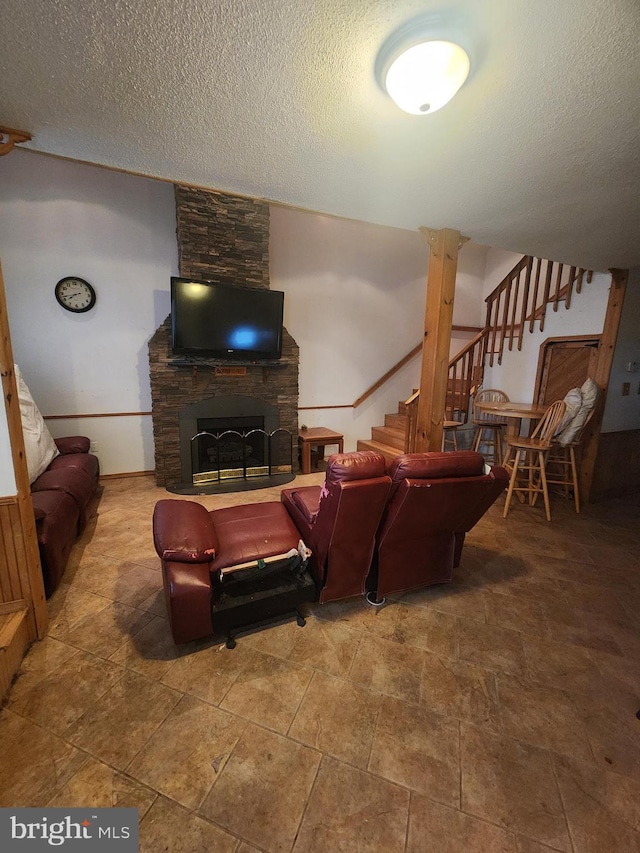 living room featuring a textured ceiling, a stone fireplace, and stairway