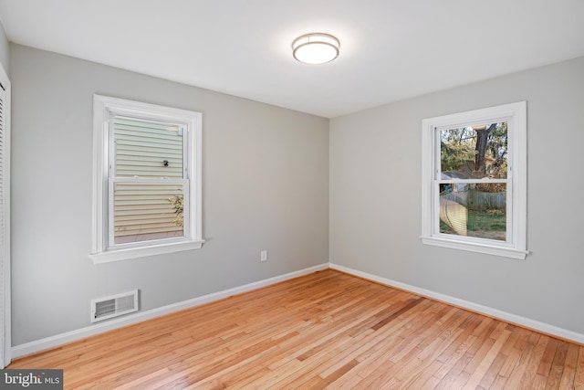 unfurnished room with hardwood / wood-style floors, visible vents, and baseboards