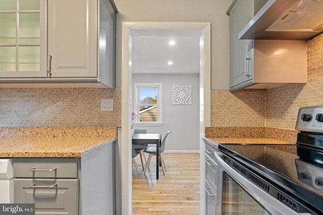 kitchen with light stone countertops, light wood-style floors, electric stove, range hood, and decorative backsplash