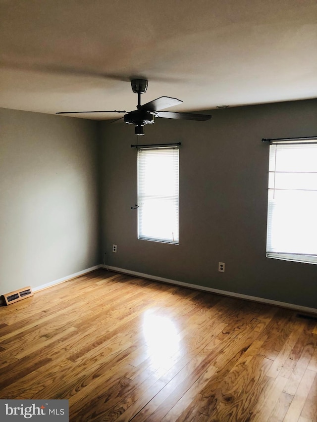 empty room featuring a ceiling fan, visible vents, baseboards, and wood finished floors