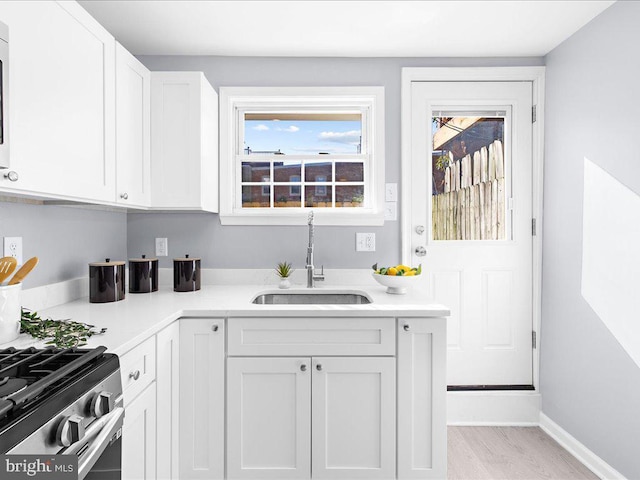 kitchen with light countertops, a sink, white cabinetry, and baseboards