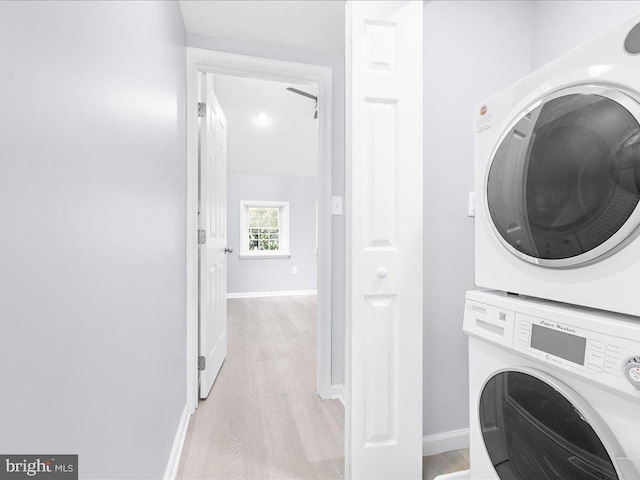 washroom featuring stacked washing maching and dryer, baseboards, laundry area, and light wood-style floors