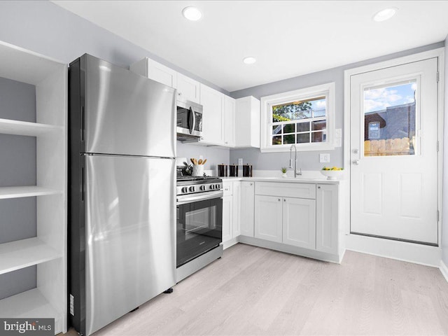 kitchen featuring stainless steel appliances, light countertops, light wood-style floors, white cabinets, and a sink