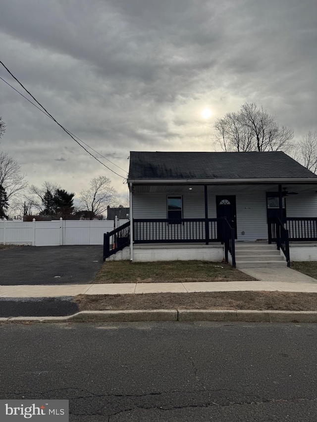 bungalow-style house with covered porch, roof with shingles, and fence