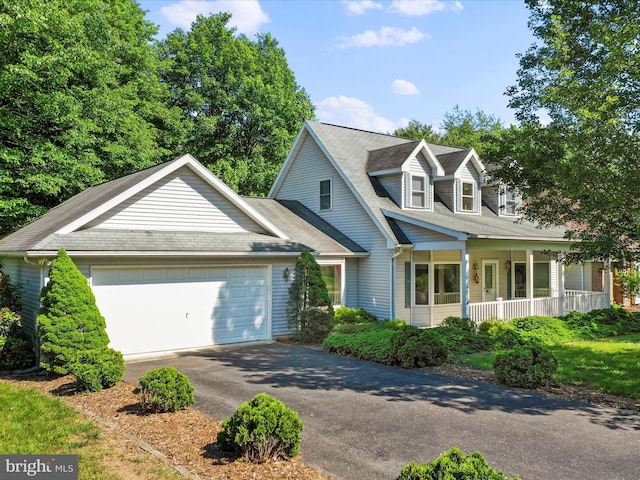 new england style home with aphalt driveway, covered porch, and an attached garage