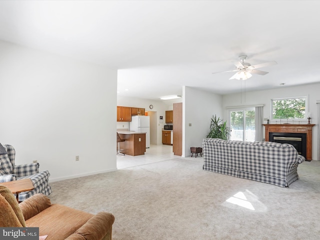 living area featuring light colored carpet, a fireplace, baseboards, and ceiling fan