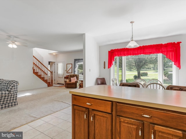 kitchen with brown cabinets, light countertops, light colored carpet, open floor plan, and light tile patterned flooring