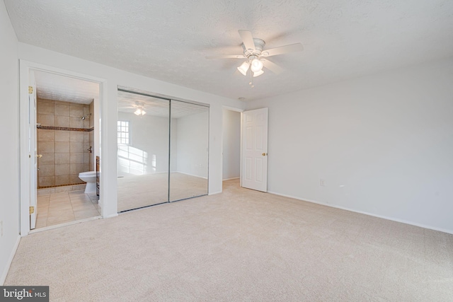 unfurnished bedroom featuring a textured ceiling, ceiling fan, connected bathroom, carpet floors, and a closet