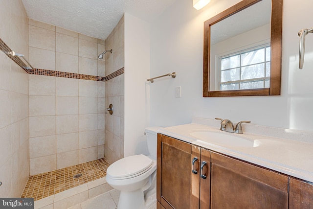 bathroom with toilet, a tile shower, a textured ceiling, vanity, and tile patterned floors