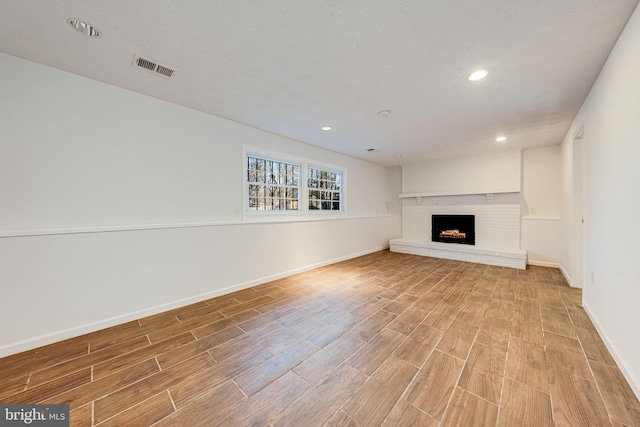 unfurnished living room with wood tiled floor, a brick fireplace, visible vents, and baseboards