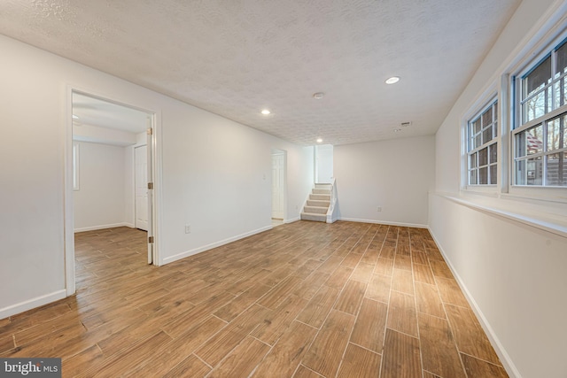 interior space featuring baseboards, stairway, light wood finished floors, and a textured ceiling