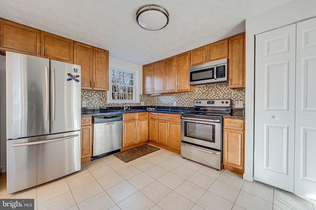 kitchen featuring brown cabinets, stainless steel appliances, dark countertops, backsplash, and a sink