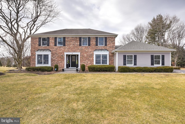 colonial inspired home featuring roof with shingles, brick siding, and a front lawn