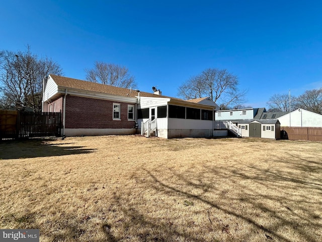 back of property with a sunroom, fence, a yard, an outdoor structure, and brick siding