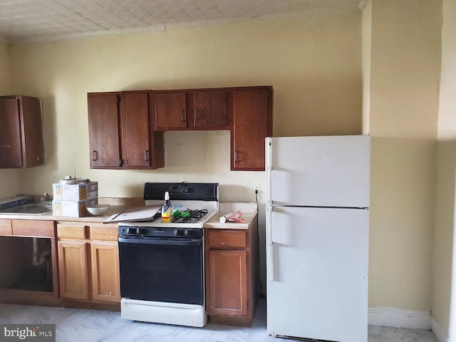 kitchen with marble finish floor, light countertops, freestanding refrigerator, brown cabinets, and gas stove