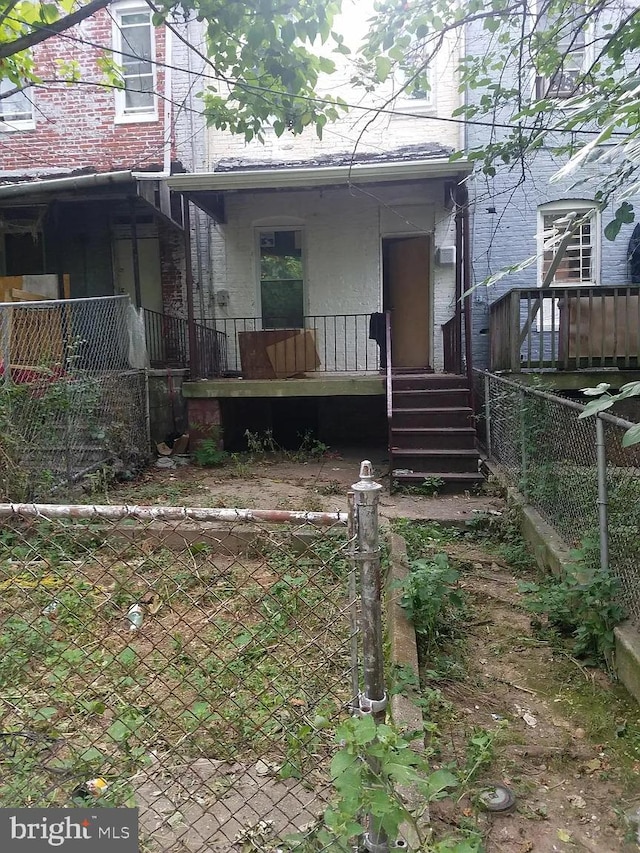 rear view of property with covered porch, brick siding, and fence