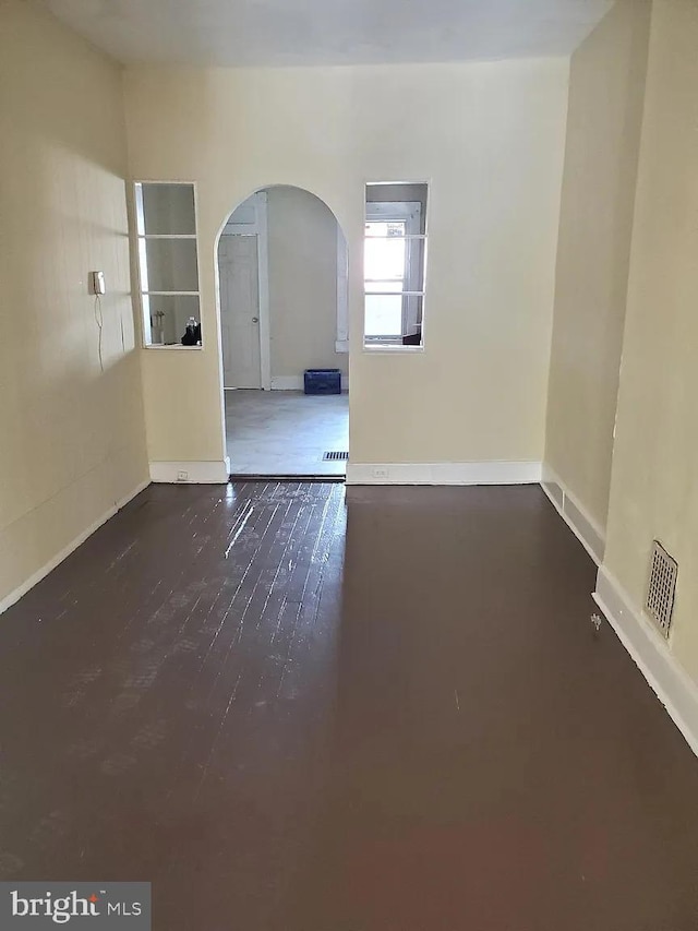 unfurnished room featuring arched walkways, visible vents, baseboards, and wood finished floors