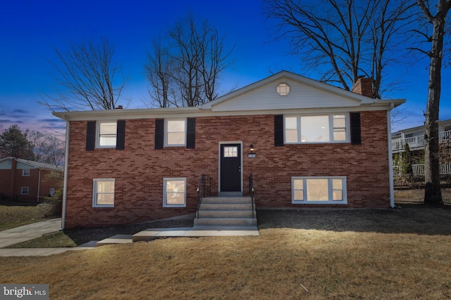 raised ranch with a yard, brick siding, and a chimney