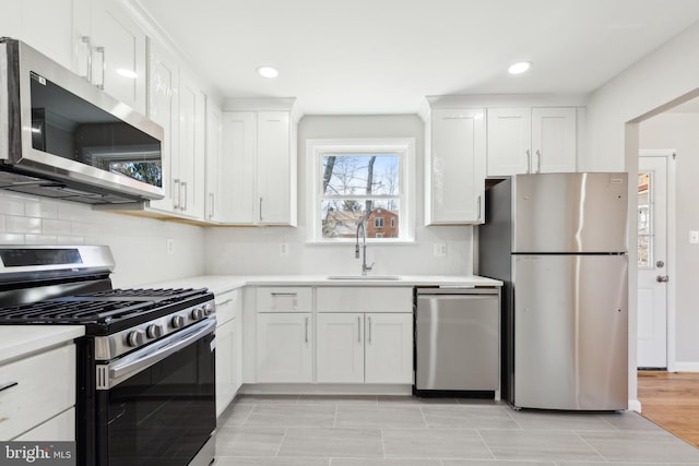 kitchen with a sink, stainless steel appliances, light countertops, white cabinetry, and backsplash