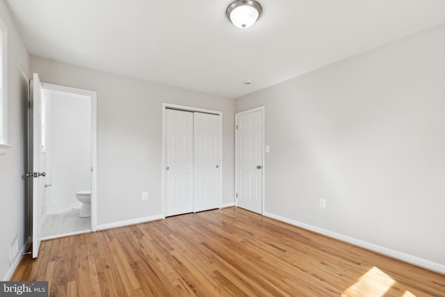 unfurnished bedroom with ensuite bathroom, light wood-style floors, baseboards, and a closet