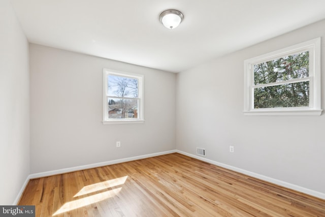 unfurnished room with plenty of natural light, wood finished floors, visible vents, and baseboards