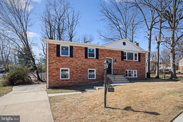 split foyer home featuring a front yard, brick siding, concrete driveway, and a chimney