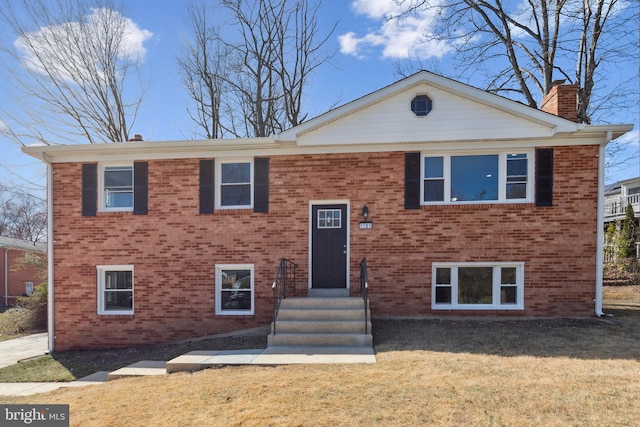 split foyer home featuring brick siding, a front yard, and a chimney