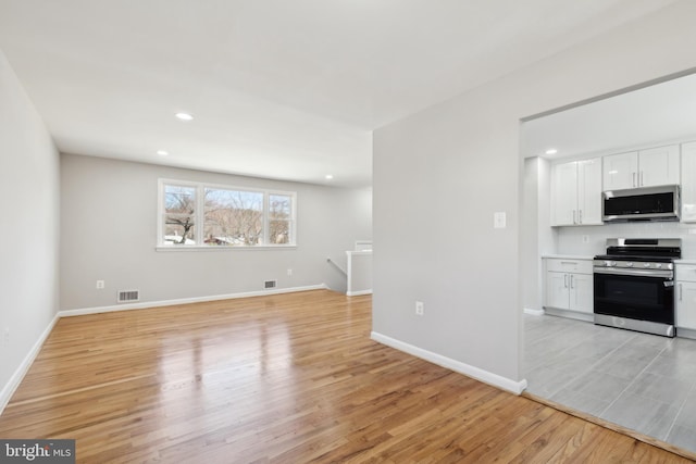 interior space with visible vents, open floor plan, light wood-style flooring, white cabinets, and stainless steel appliances