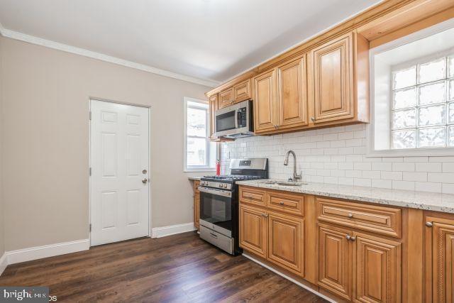 kitchen with light stone counters, dark wood-style flooring, ornamental molding, appliances with stainless steel finishes, and backsplash