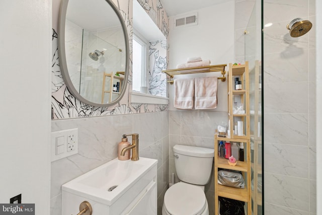 bathroom with toilet, vanity, visible vents, tile walls, and tiled shower