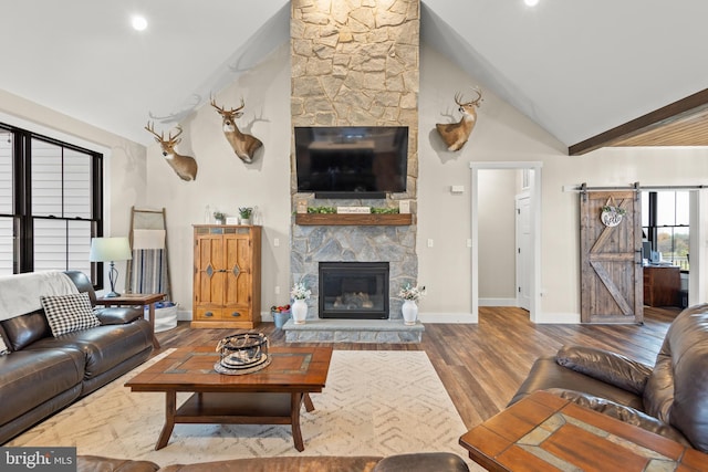 living room featuring high vaulted ceiling, a barn door, a fireplace, wood finished floors, and baseboards