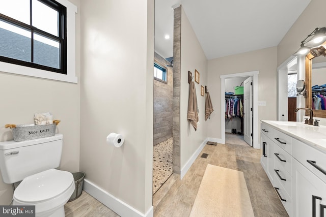 bathroom with a walk in shower, toilet, wood finished floors, vanity, and baseboards