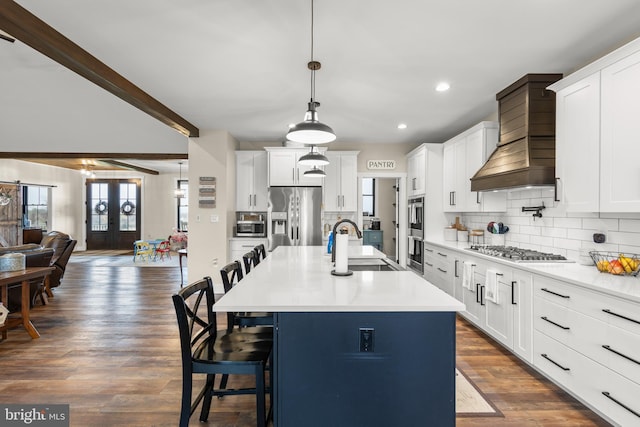 kitchen with a sink, open floor plan, appliances with stainless steel finishes, custom exhaust hood, and tasteful backsplash