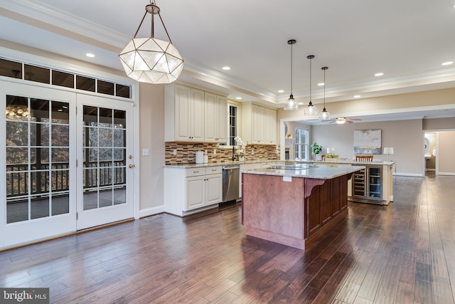 kitchen featuring a tray ceiling, dark wood-style flooring, stainless steel dishwasher, a kitchen island, and light stone countertops