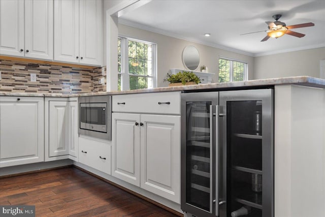 kitchen with beverage cooler, white cabinets, ornamental molding, stainless steel microwave, and dark wood finished floors