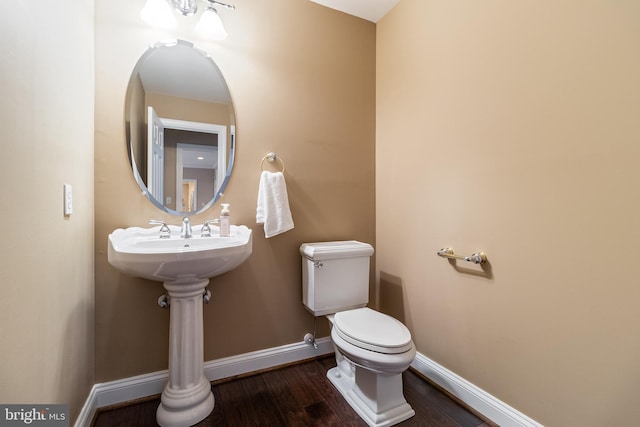 half bath with toilet, baseboards, and wood finished floors