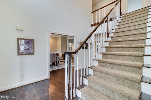 staircase featuring ornamental molding, baseboards, a high ceiling, and hardwood / wood-style floors