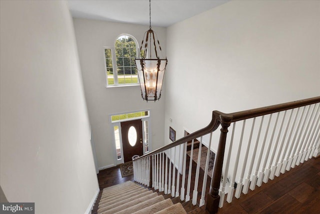 stairs with a chandelier, wood finished floors, and baseboards