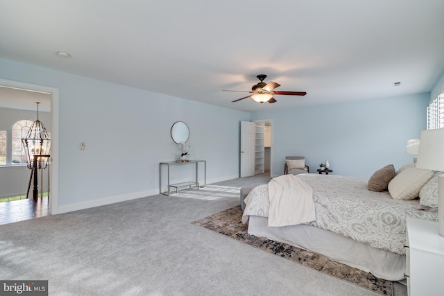 carpeted bedroom featuring baseboards and ceiling fan with notable chandelier