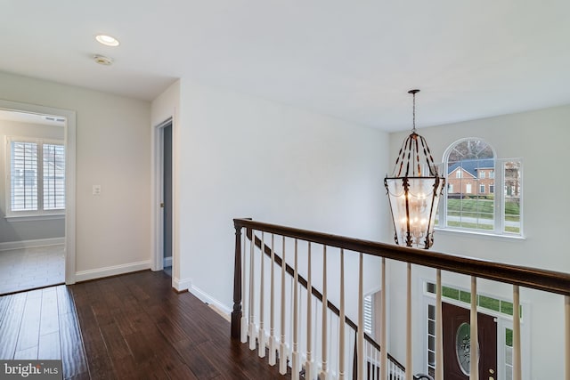 hall featuring a healthy amount of sunlight, an inviting chandelier, dark wood finished floors, and an upstairs landing