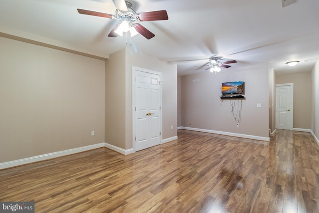 empty room with a ceiling fan, wood finished floors, visible vents, and baseboards