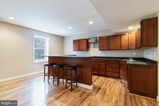 kitchen with recessed lighting, a sink, baseboards, light wood-style floors, and a kitchen bar