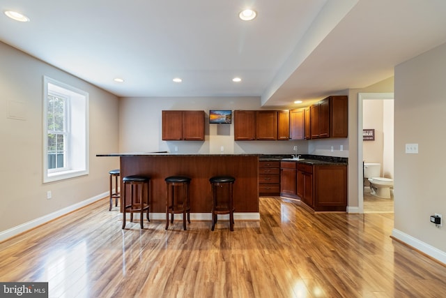 kitchen featuring light wood finished floors, dark countertops, a kitchen bar, and recessed lighting