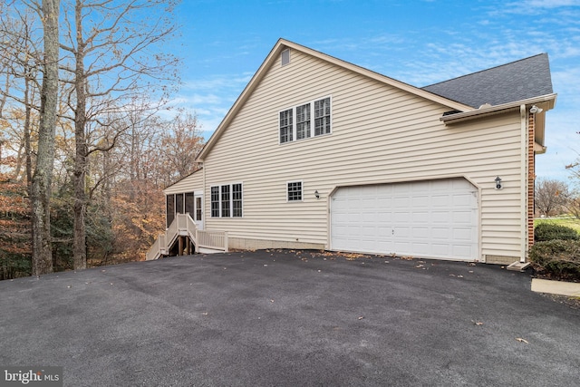 view of side of home with a garage, a shingled roof, and aphalt driveway