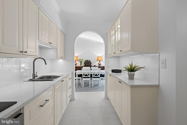 kitchen featuring glass insert cabinets, ornamental molding, a sink, black electric stovetop, and backsplash