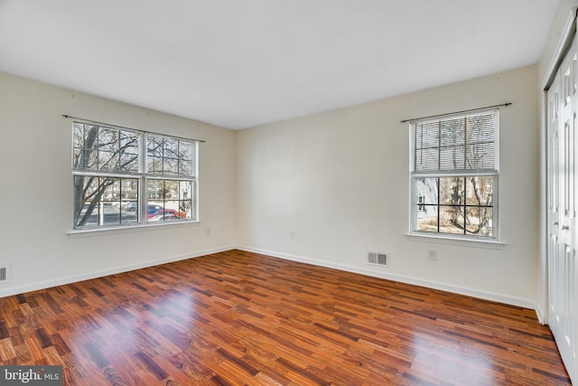 empty room featuring wood finished floors, visible vents, and a healthy amount of sunlight